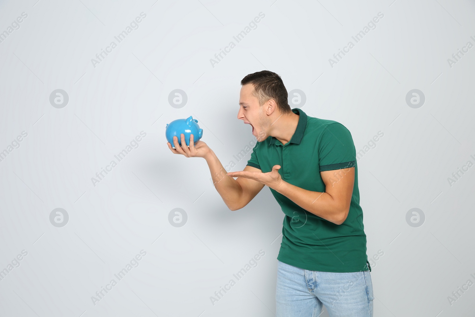 Photo of Emotional young man with piggy bank on white background. Space for text