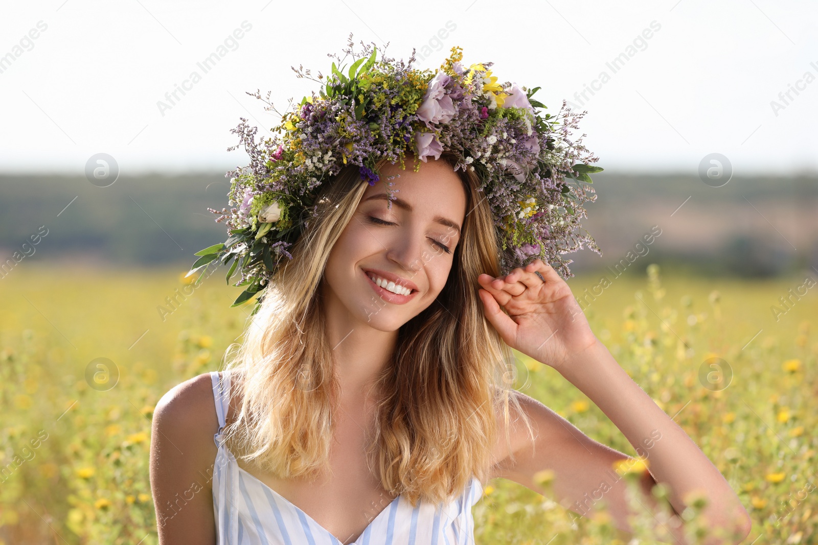 Photo of Young woman wearing wreath made of beautiful flowers in field on sunny day