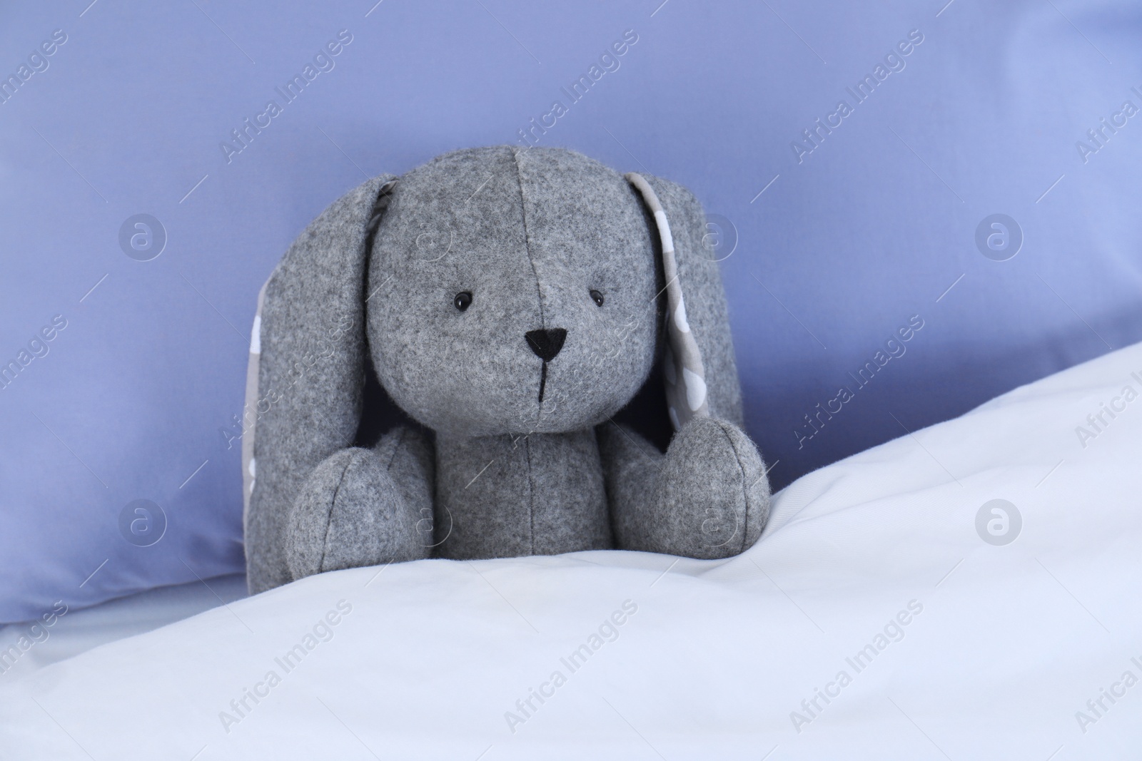 Photo of Cute toy rabbit lying in bed indoors. Space for text