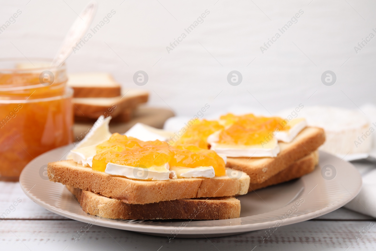 Photo of Tasty sandwiches with brie cheese and apricot jam on white wooden table, closeup