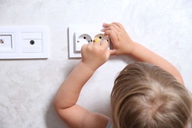 Little child playing with toy screwdriver and electrical socket at home, closeup. Dangerous situation