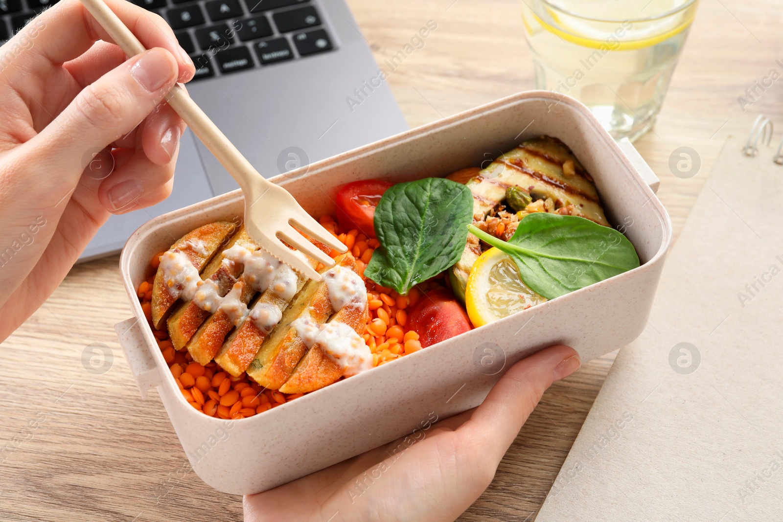 Photo of Woman eating healthy products high in vegetable fats near laptop at wooden table, closeup