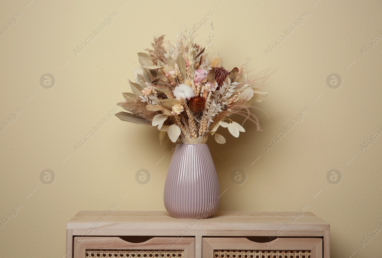 Photo of Beautiful dried flower bouquet in ceramic vase on wooden table near beige wall