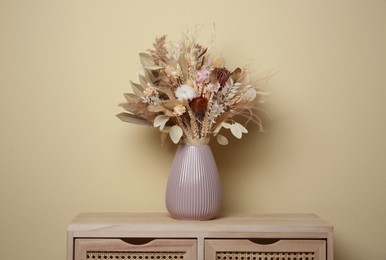 Beautiful dried flower bouquet in ceramic vase on wooden table near beige wall