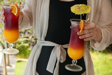 Photo of Woman holding glasses with delicious cocktails outdoors
