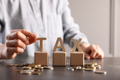 Photo of Woman with word Tax, wooden cubes and coins at grey table, closeup