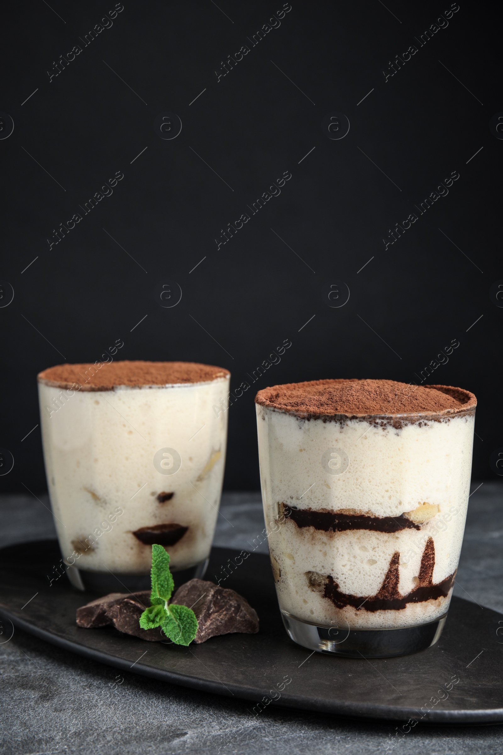 Photo of Two glasses of tiramisu cake on table against dark background