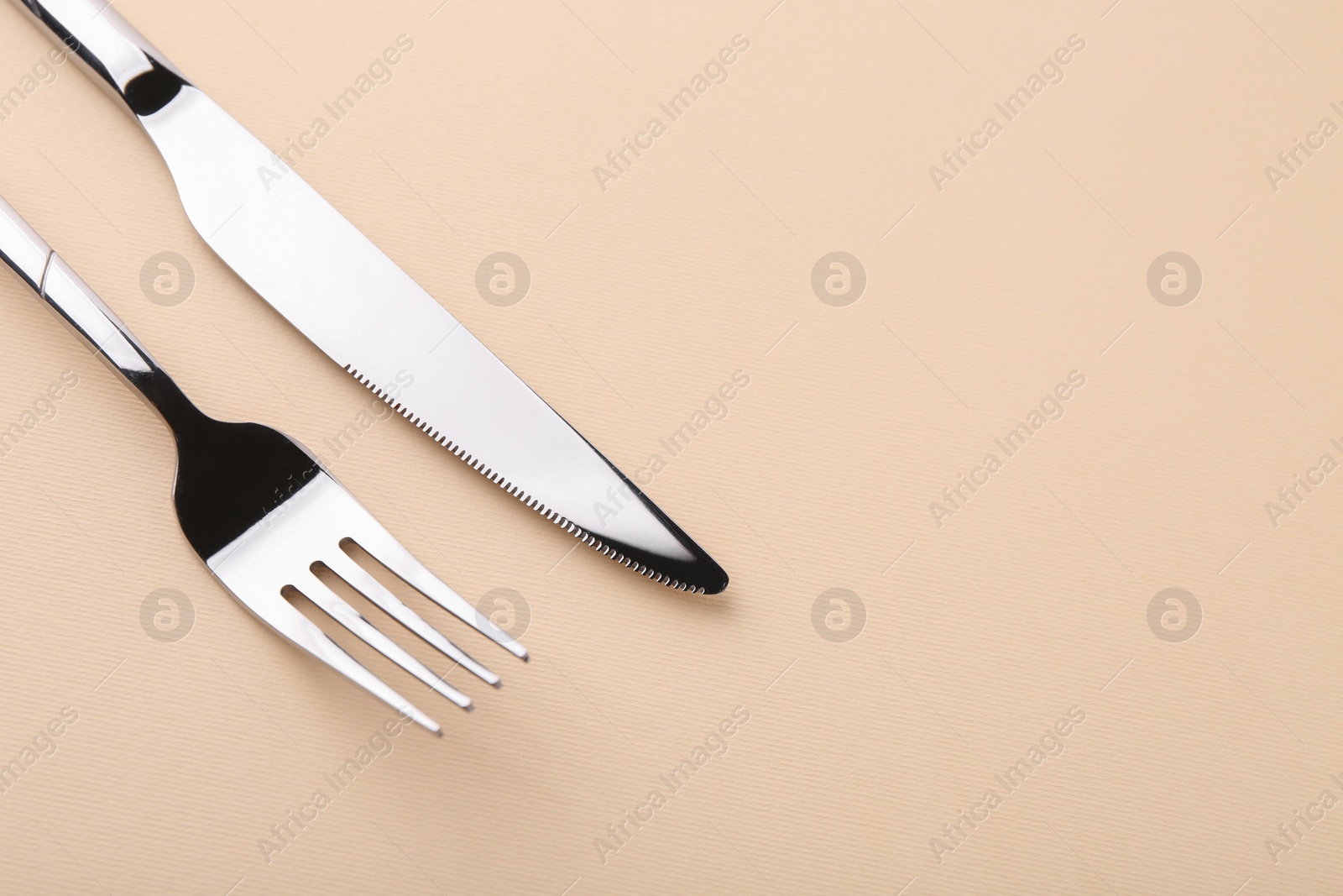 Photo of Stylish cutlery. Silver knife and fork on beige background, above view. Space for text