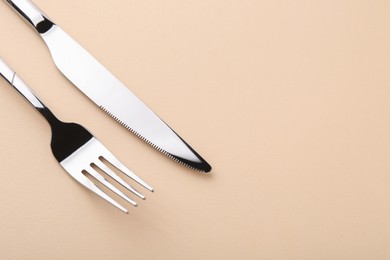 Stylish cutlery. Silver knife and fork on beige background, above view. Space for text