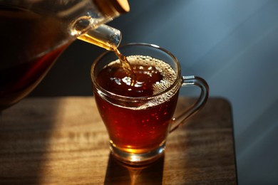 Photo of Pouring delicious tea into glass cup on wooden table, closeup