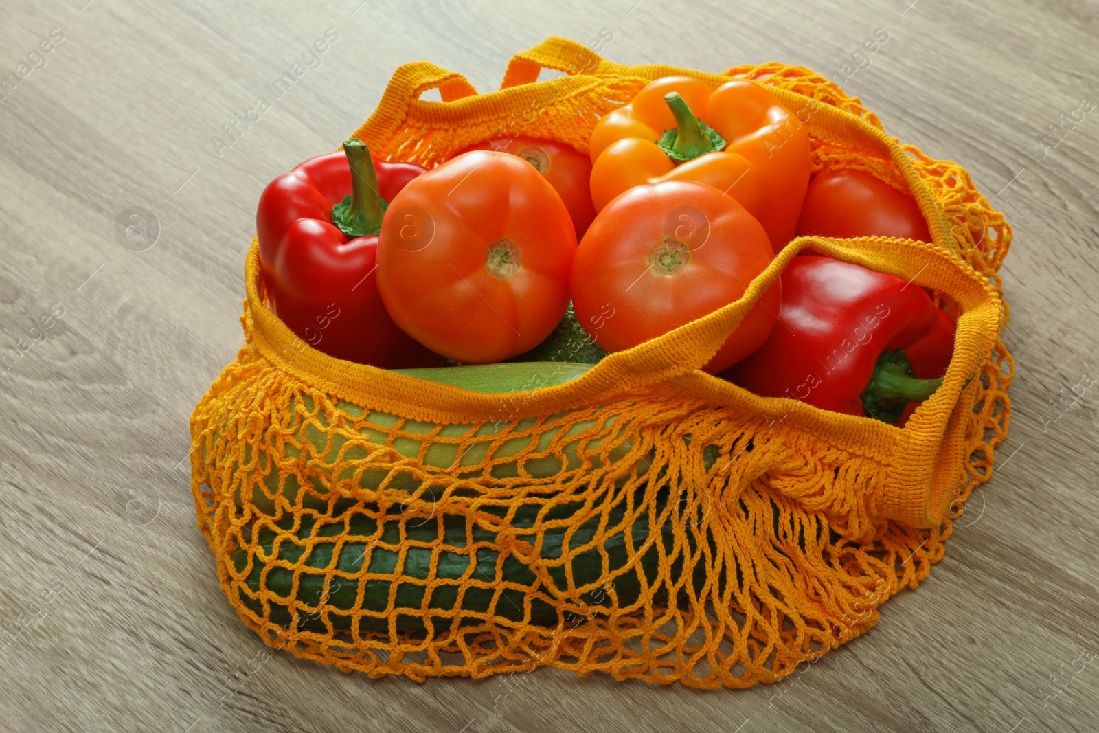 Photo of Net bag with vegetables on wooden table