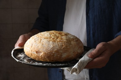 Photo of Man holding loaf of fresh bread on dark background, closeup