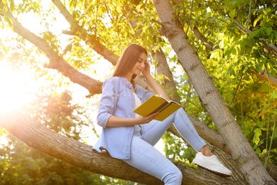 Photo of Young woman reading book on tree in park