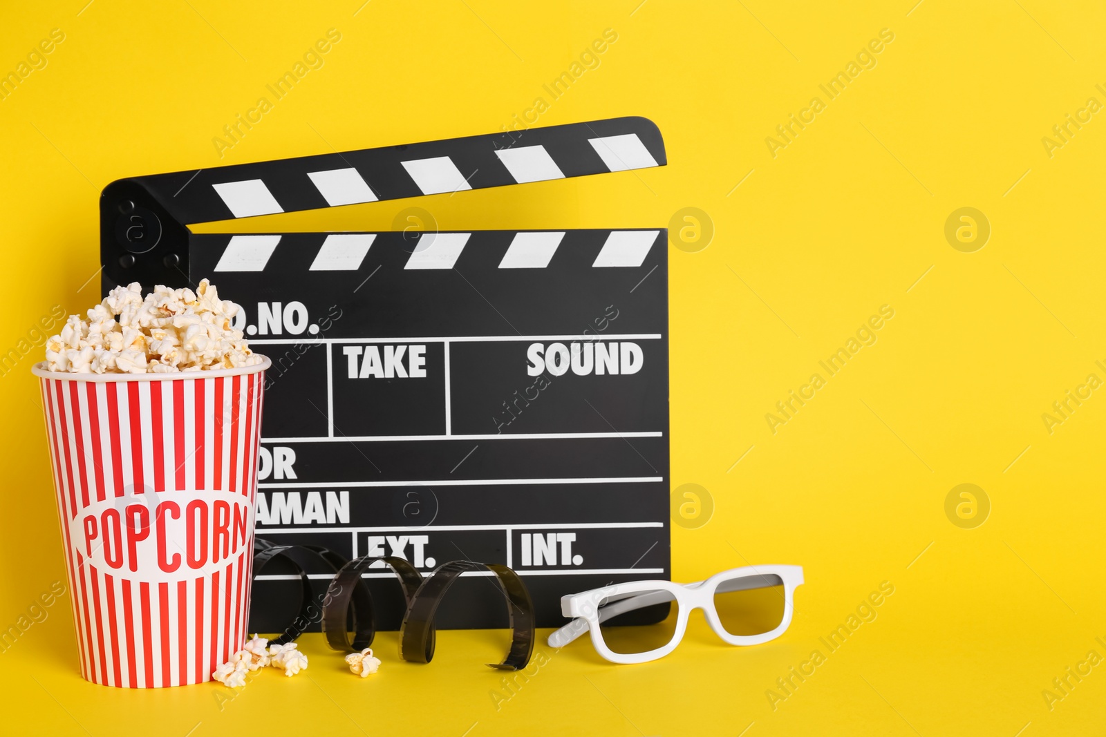 Photo of Delicious popcorn, 3D glasses, tape and clapperboard on yellow background