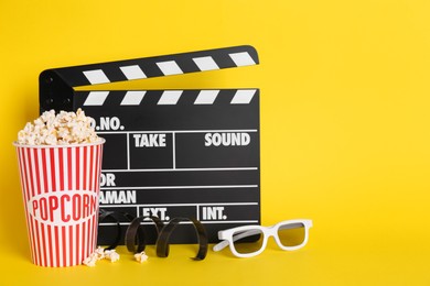 Delicious popcorn, 3D glasses, tape and clapperboard on yellow background