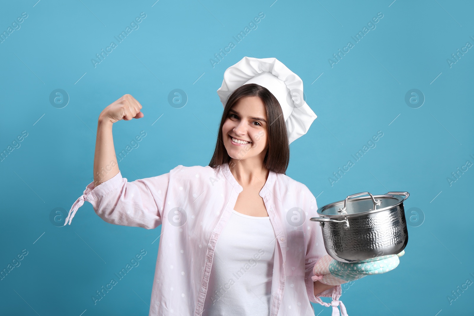 Photo of Happy young woman with cooking pot on light blue background