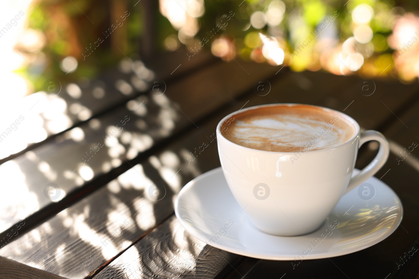 Photo of Cup of aromatic coffee with foam on table in outdoor cafe. Space for text