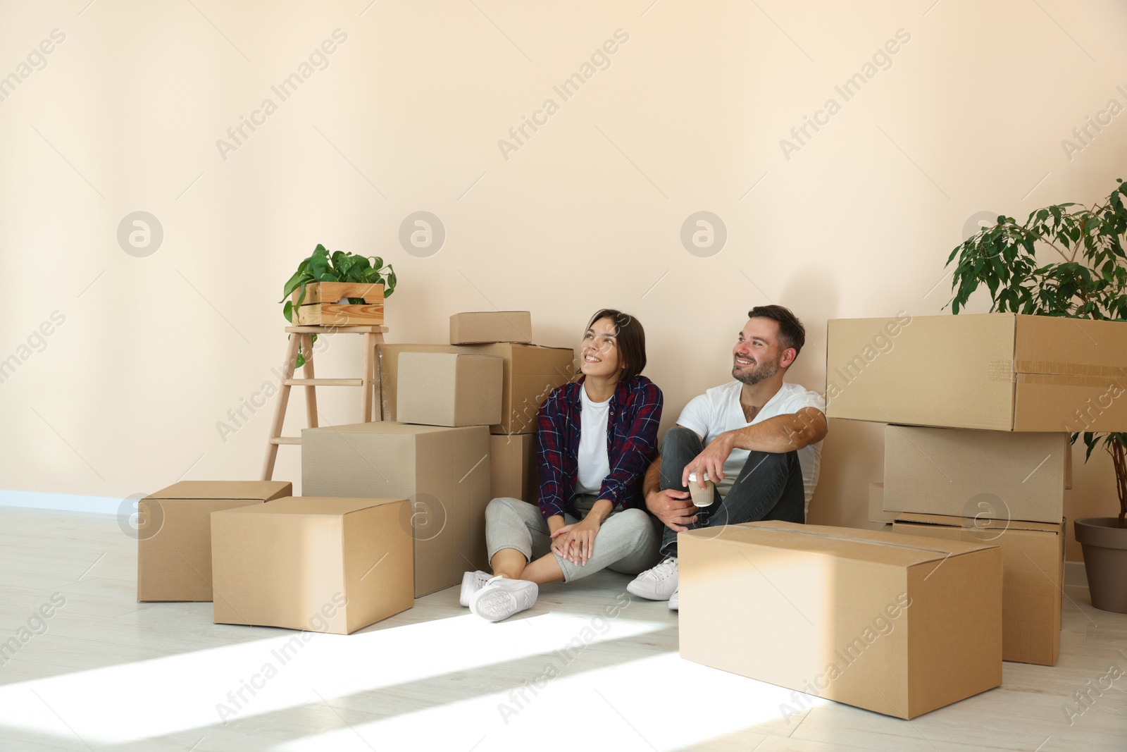 Photo of Happy couple with takeaway coffee resting on floor in new apartment. Moving day