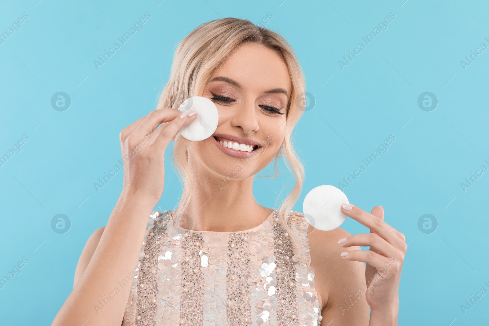 Photo of Smiling woman removing makeup with cotton pads on light blue background