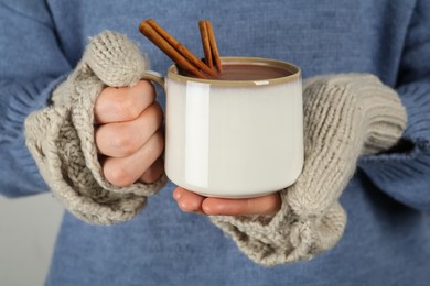 Photo of Woman in fingerless mittens holding cup of delicious hot chocolate with cinnamon sticks, closeup