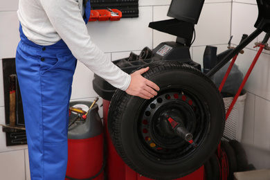 Mechanic working with wheel balancing machine at tire service, closeup