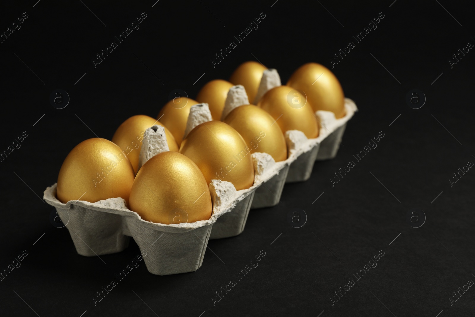 Photo of Shiny golden eggs in box on black background