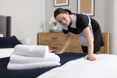 Photo of Young maid making bed in hotel room, selective focus