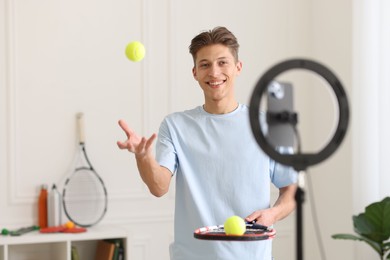 Photo of Smiling sports blogger with tennis racket and balls streaming online fitness lesson at home