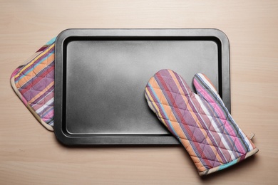 Photo of Oven potholders and baking tray on wooden table, top view