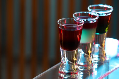 Photo of Different shooters in shot glasses on surface against blurred background, closeup and space for text Alcohol drink