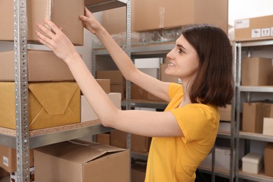 Post office worker putting box on rack with parcels indoors