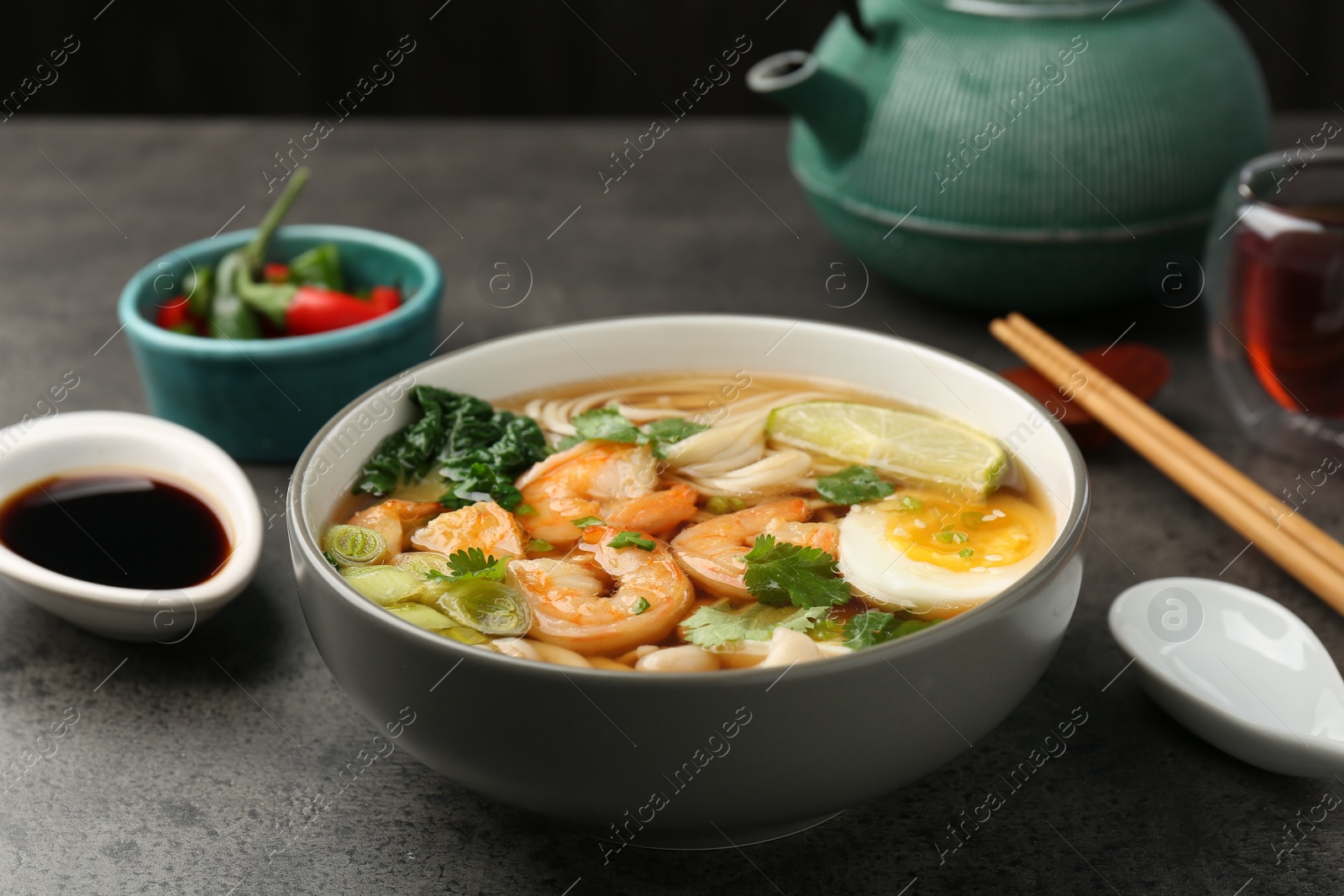 Photo of Delicious ramen with shrimps and egg in bowl served on grey table. Noodle soup