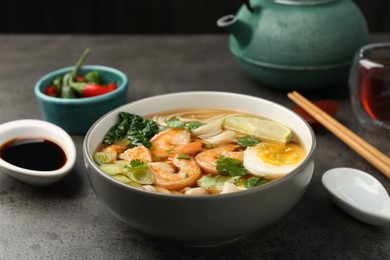 Delicious ramen with shrimps and egg in bowl served on grey table. Noodle soup