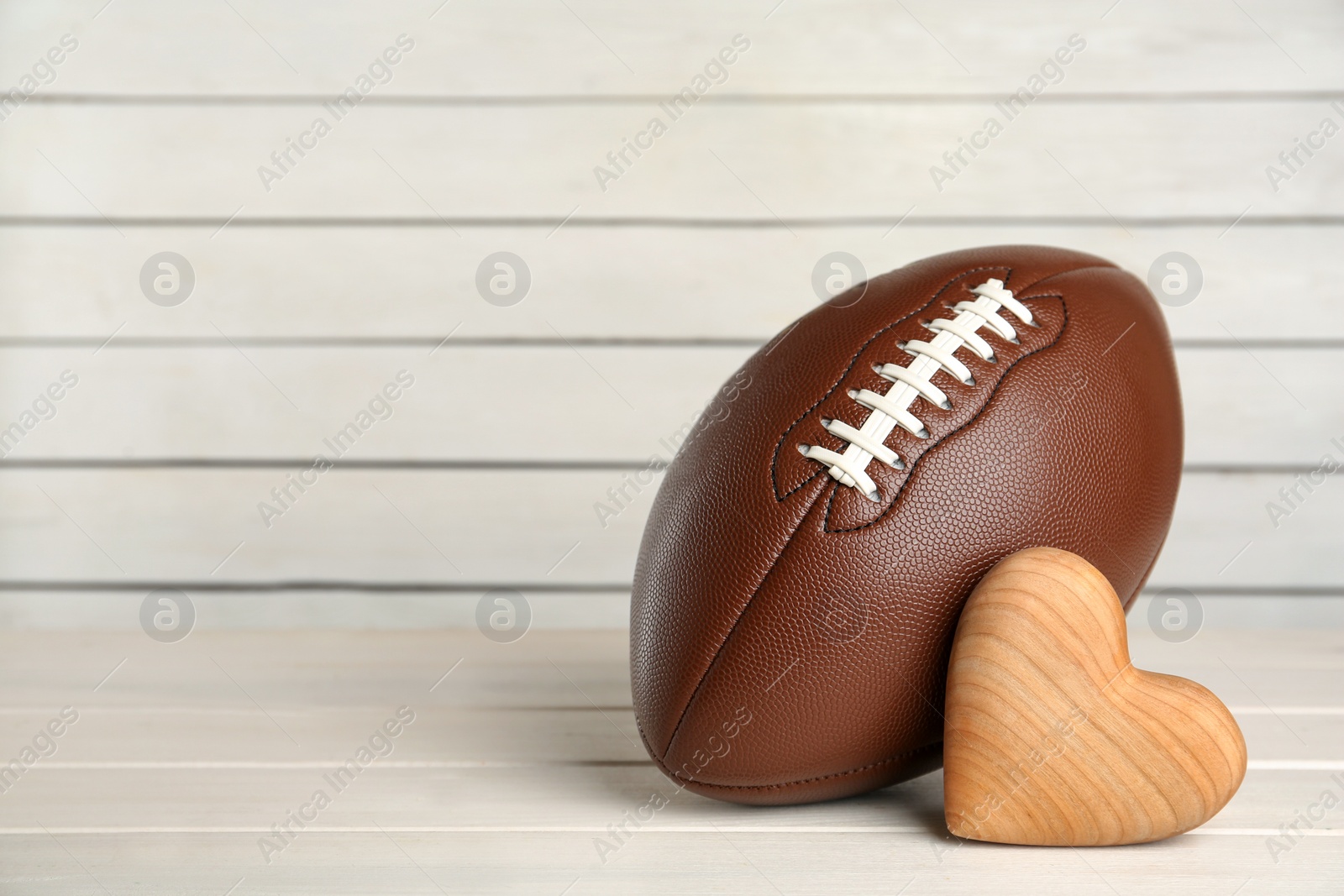 Photo of American football ball and heart on white wooden table. Space for text