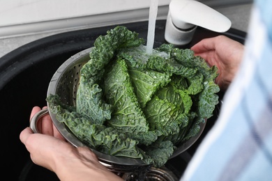 Photo of Woman washing fresh green savoy cabbage under tap water in kitchen sink, closeup