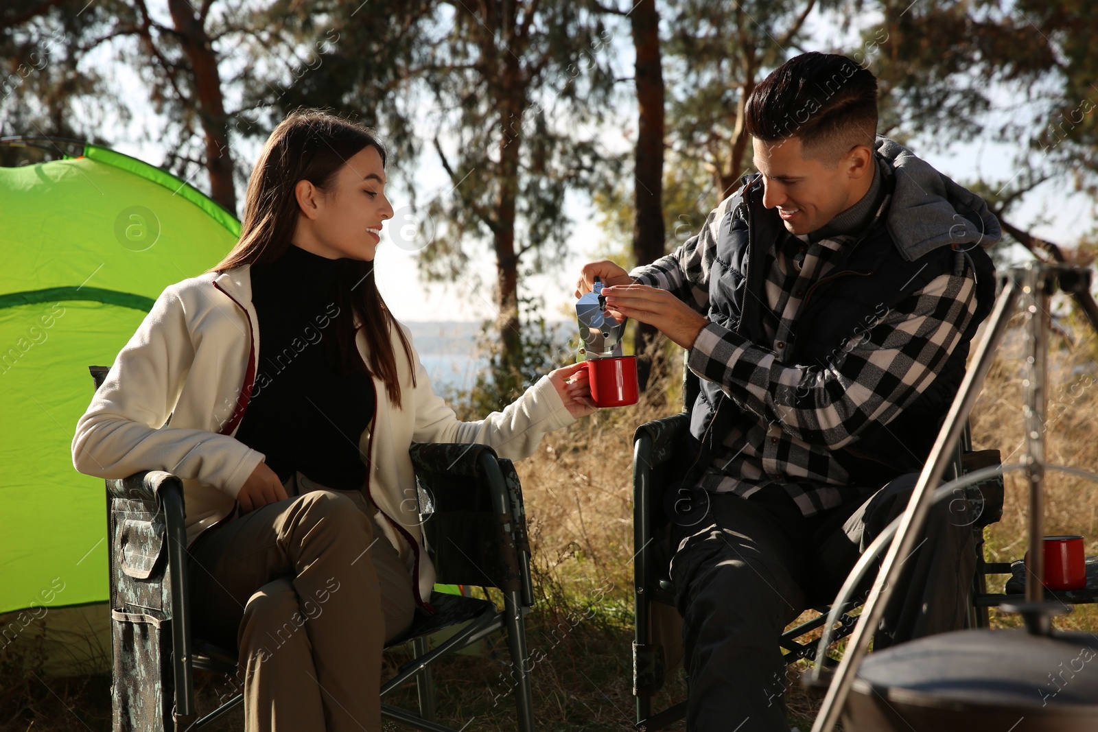 Photo of Couple resting in camping chairs and enjoying hot drink outdoors