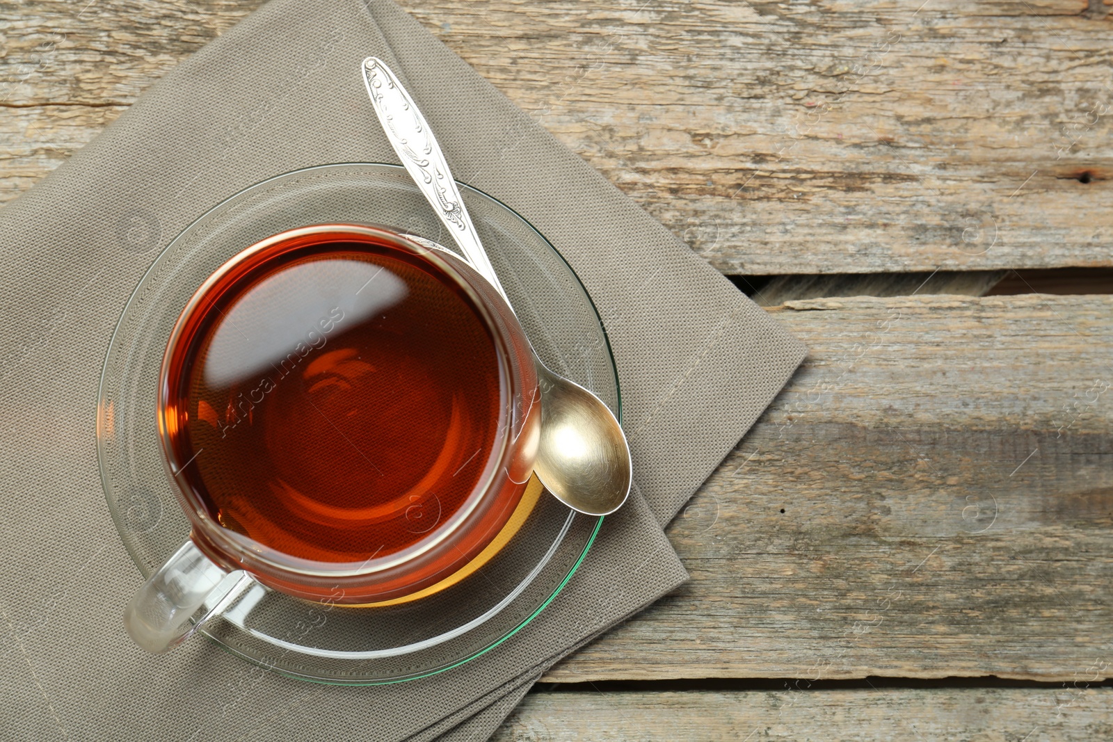 Photo of Aromatic tea in glass cup, spoon and napkin on wooden table, top view. Space for text