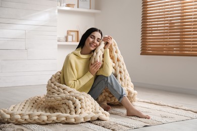 Photo of Young woman with chunky knit blanket on floor at home
