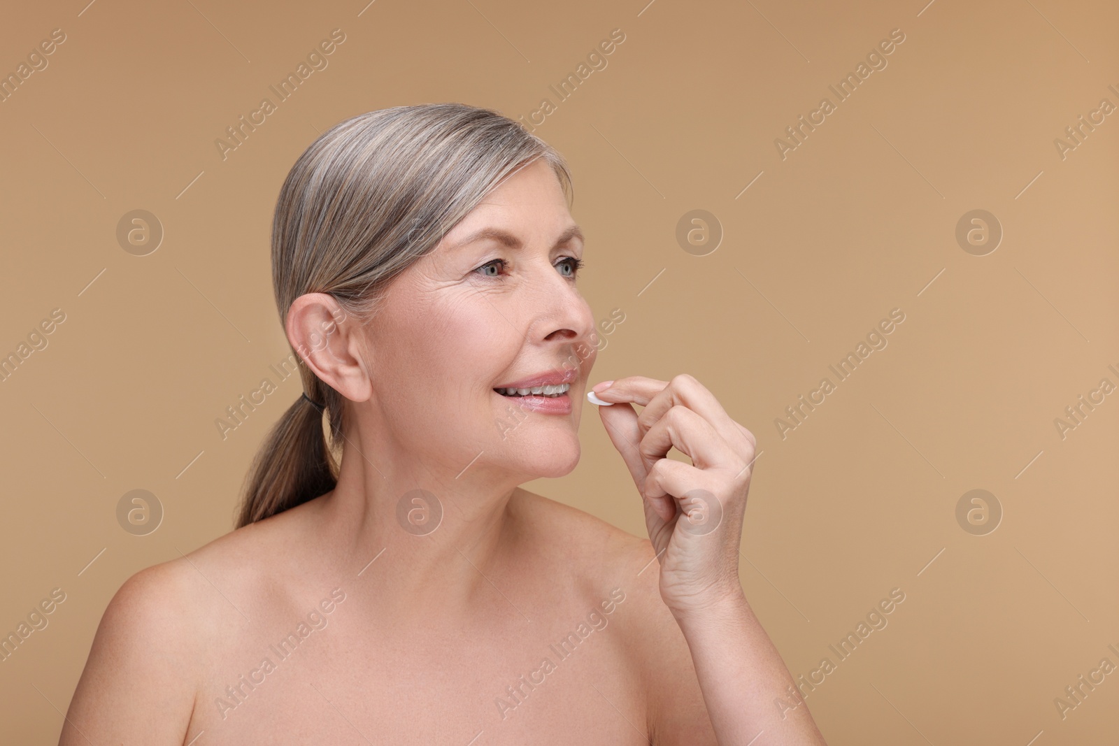 Photo of Beautiful woman taking vitamin pill on beige background, space for text