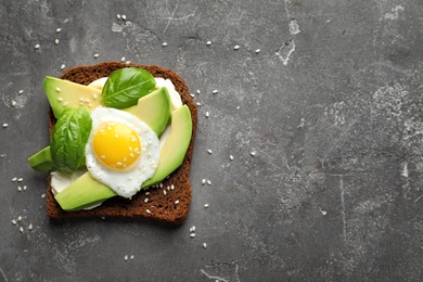 Toast bread with cream cheese, avocado and fried egg on dark background