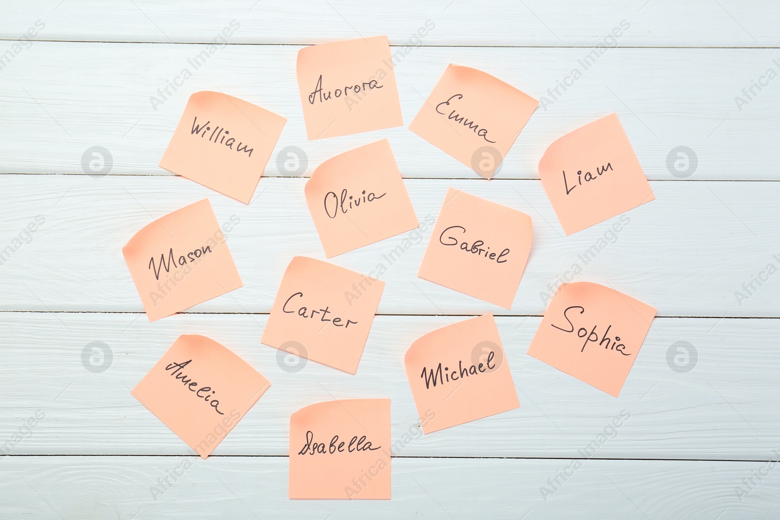 Photo of Paper stickers with different names on white wooden background, flat lay. Choosing baby's name