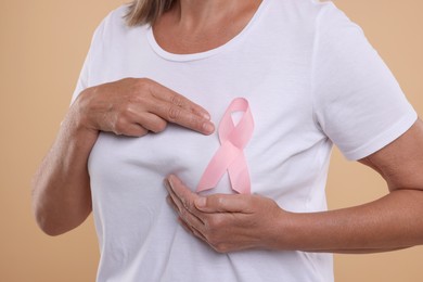 Photo of Breast cancer awareness. Woman with pink ribbon doing self-examination on light brown background, closeup