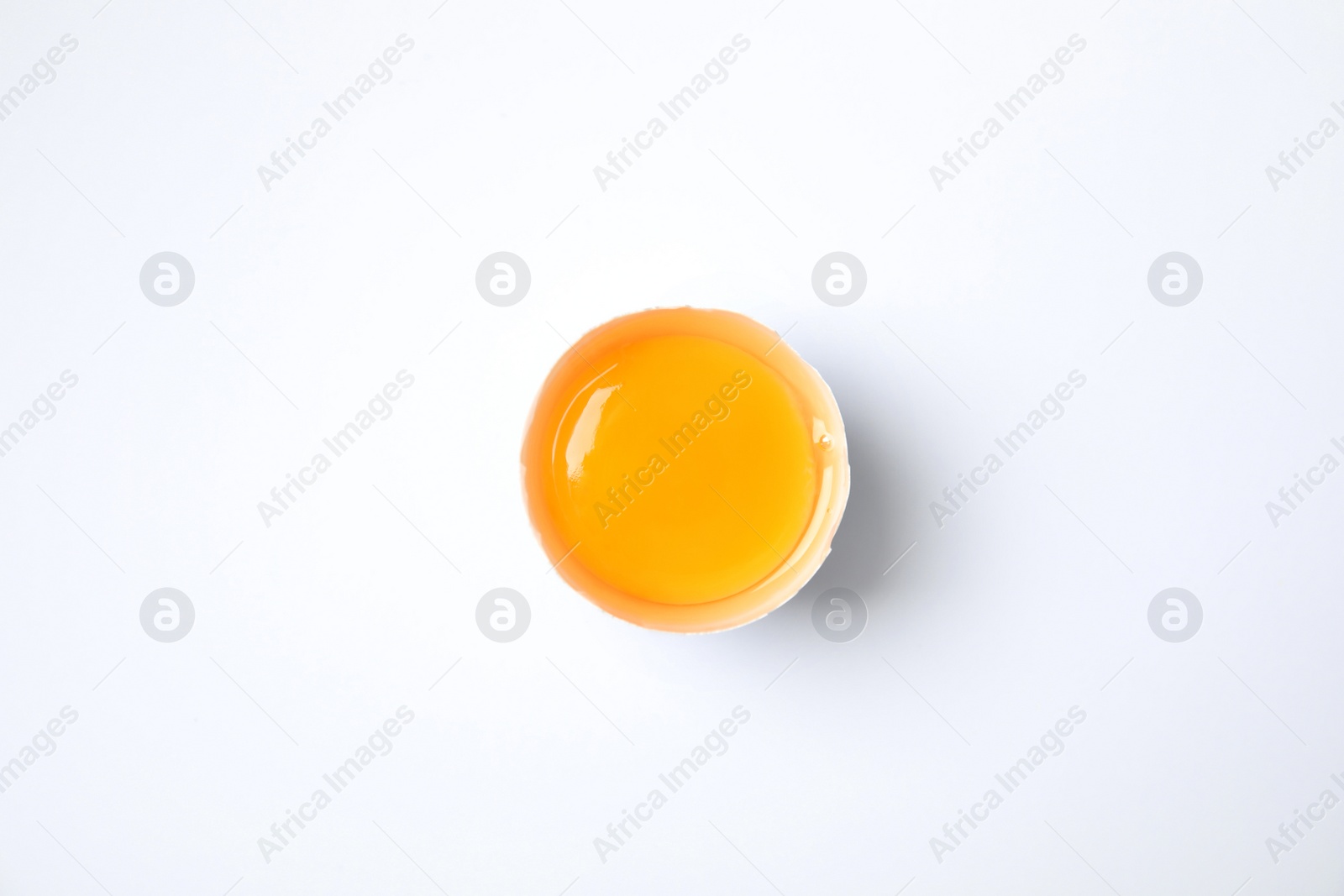 Photo of Cracked chicken egg with yolk on white background, top view