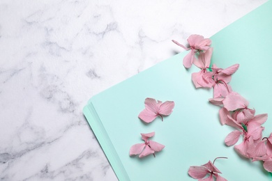 Open notebook and beautiful flowers on white marble table, flat lay. Space for text