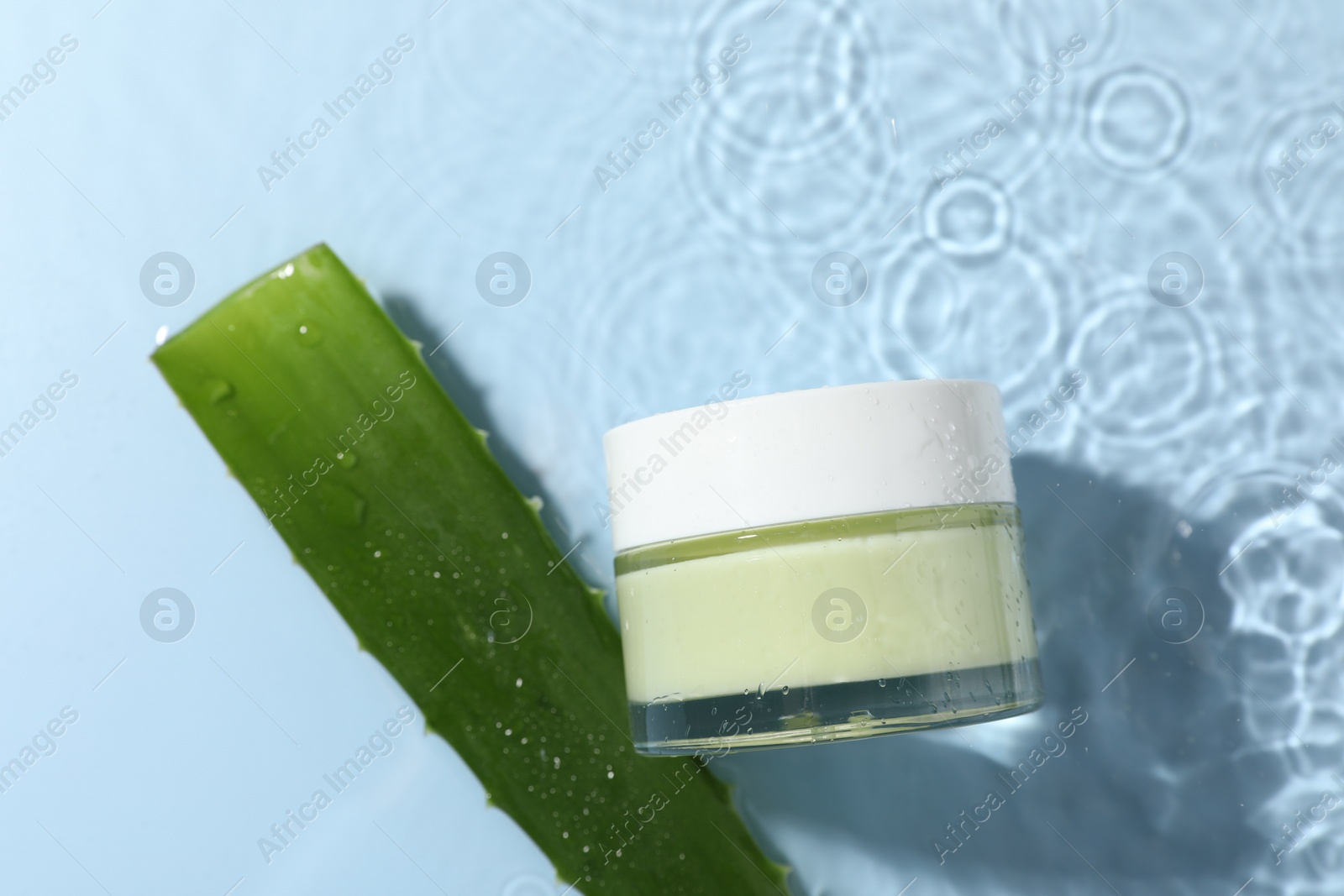 Photo of Jar of cosmetic product and aloe leaves in water on light blue background, flat lay