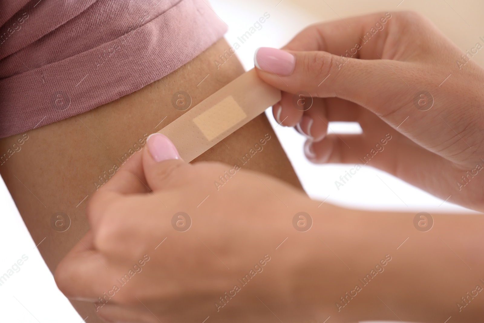 Photo of Woman applying adhesive bandage on man's arm against light background, closeup