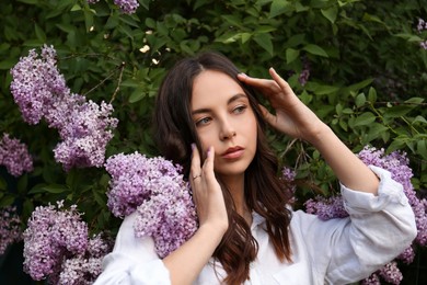 Attractive young woman near blooming lilac bush outdoors