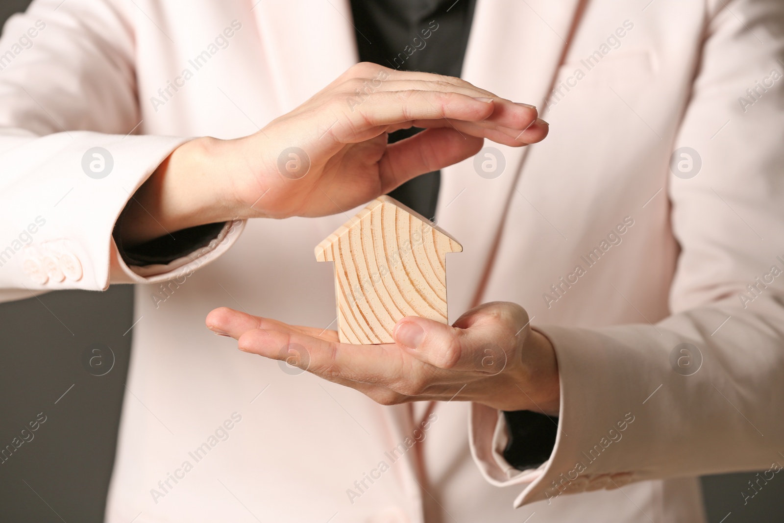 Photo of Female agent covering wooden house on dark background, closeup. Home insurance