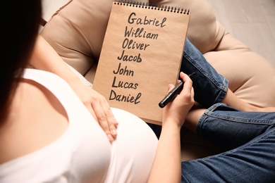 Photo of Pregnant woman with baby names list sitting in armchair, closeup