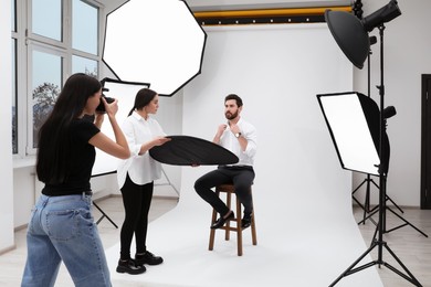 Photo of Professional photographer and assistant working with handsome model in modern photo studio